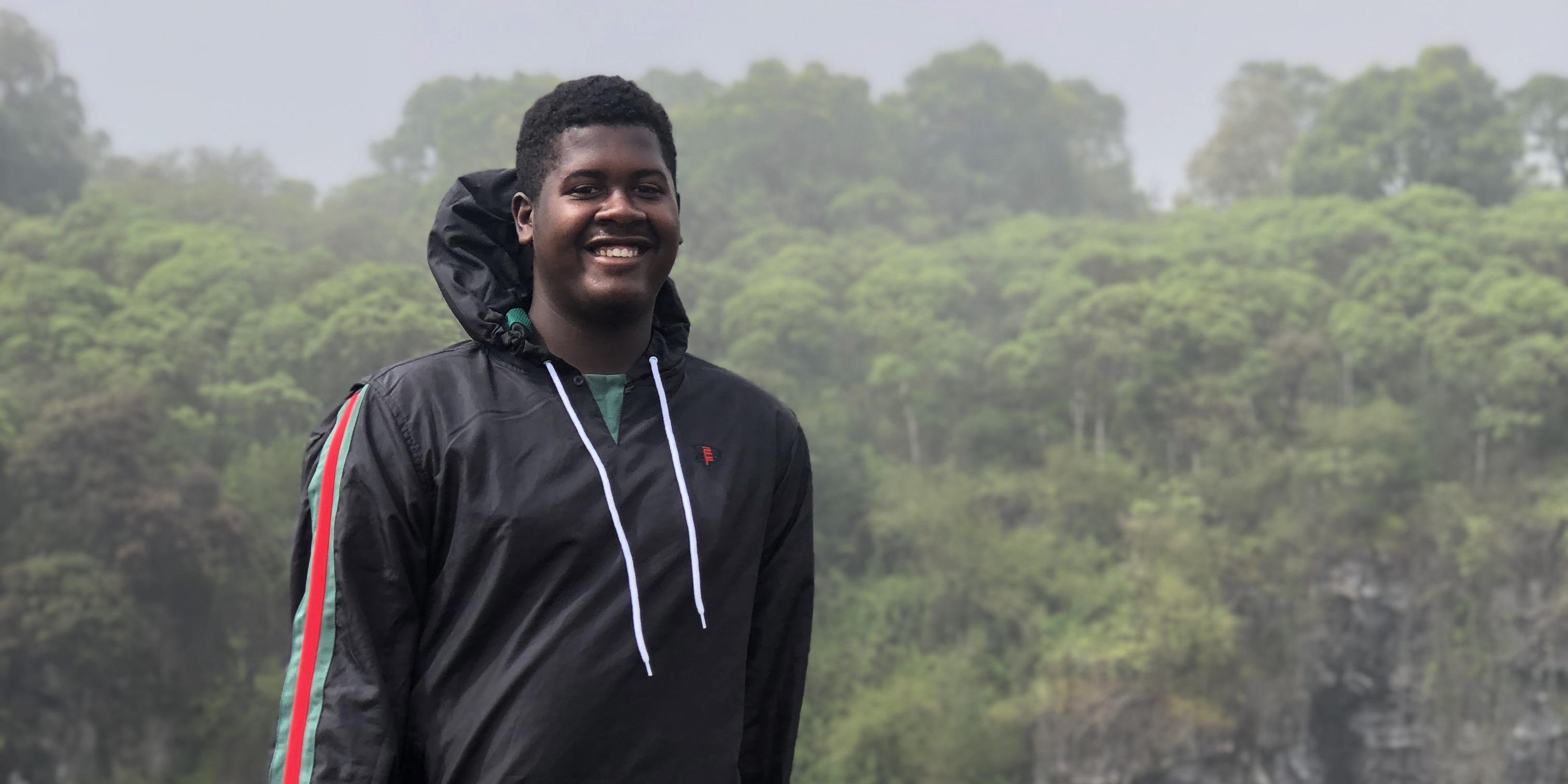 A student smiles with rainforest in the background