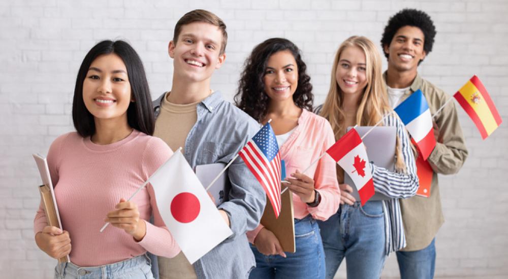 Five students standing in a line holding flags from different countries.
