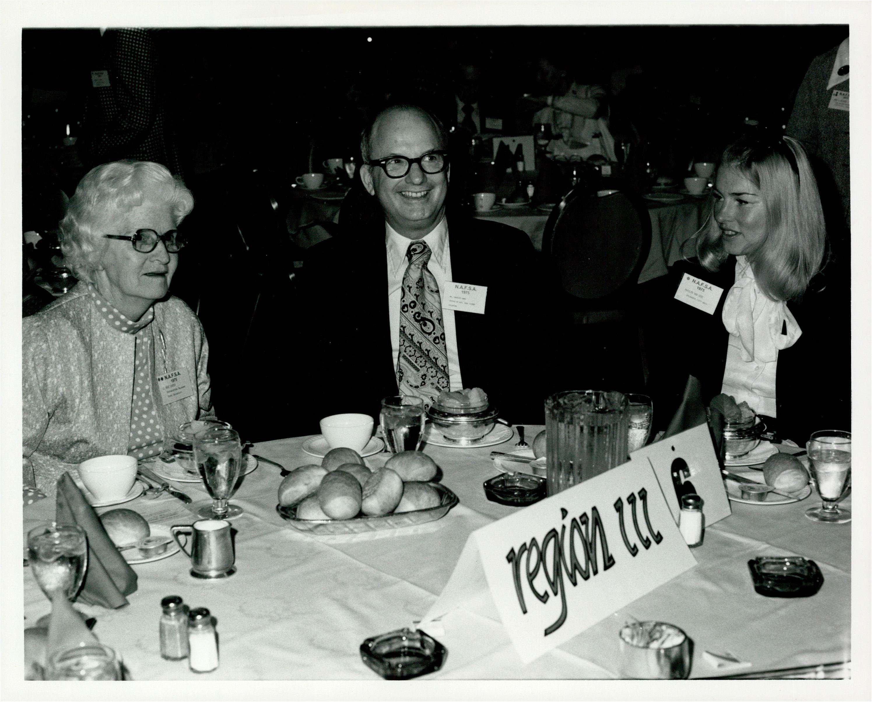 Black and white image of three people at a banquet sitting at a table with a sign that says region III