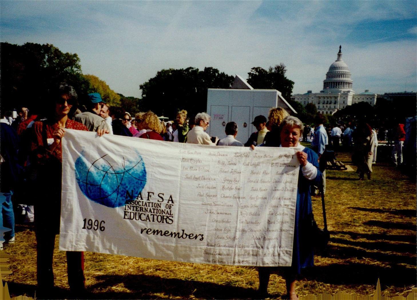 Two people holding up a flag that says NAFSA remembers, with the names of those lost to the AIDS epidemic