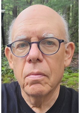 A photo of Jon Rubin wearing glasses while in the woods