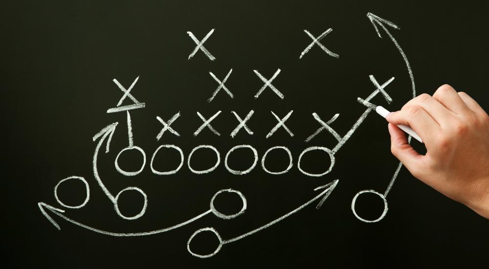Photo of a person holding chalk drawing out a football play on a dark background