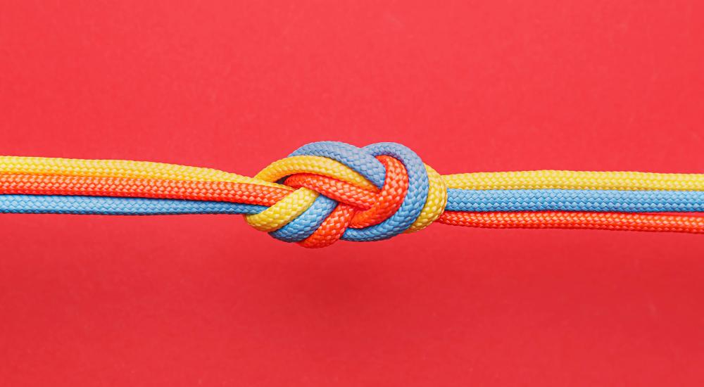 photograph of orange, blue, and yellow cords tied in knot on red background