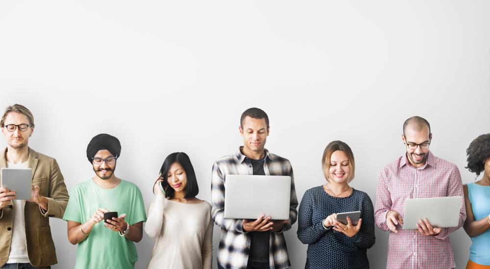 Group of people standing in a line holding technology devices.