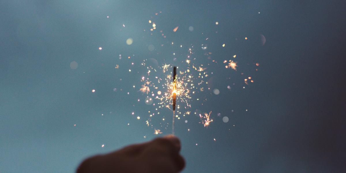 hand holding lit sparkler against dark blue backgorund