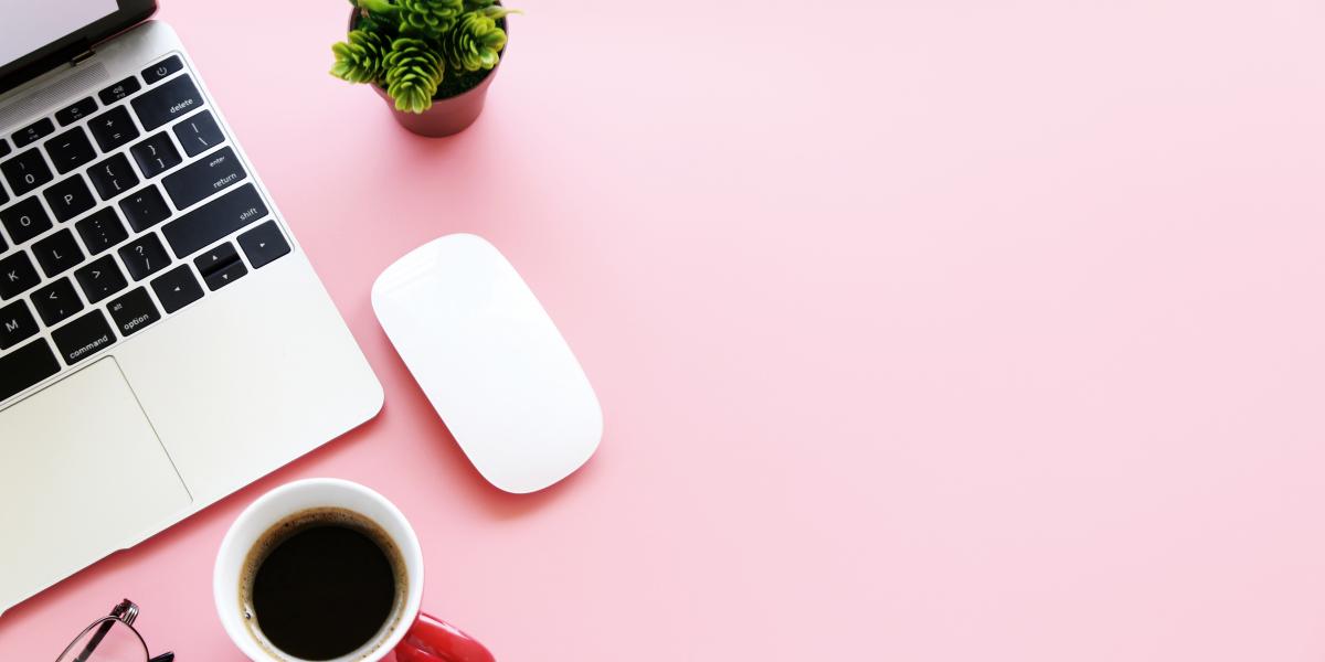 Laptop, mouse, plant, coffee cup, and glasses on a pink background