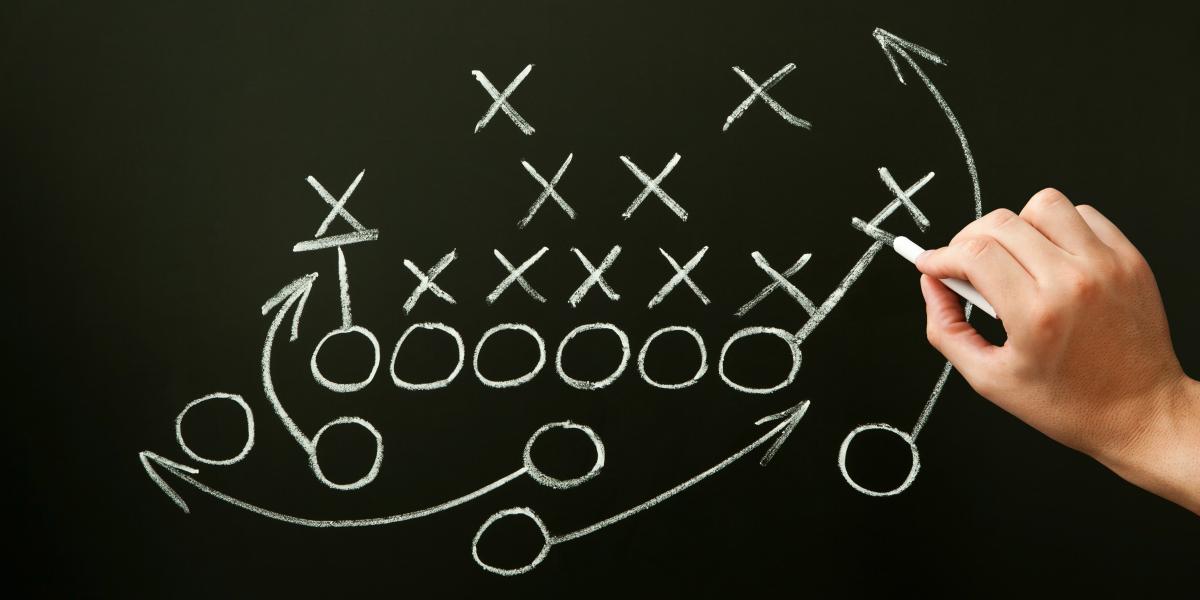 Photo of a person holding chalk drawing out a football play on a dark background