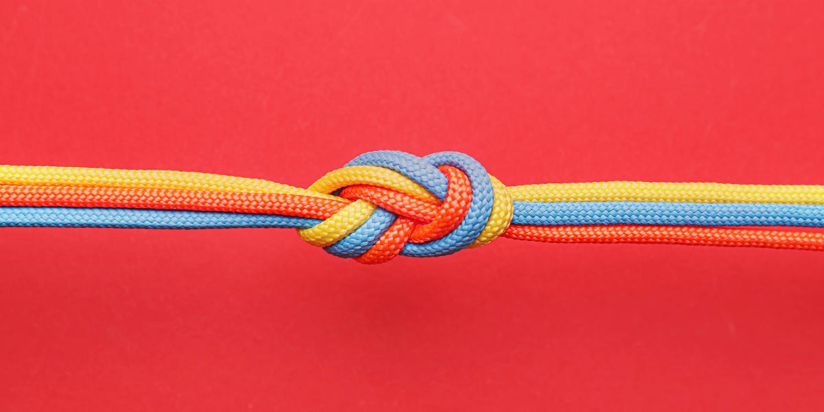 photograph of orange, blue, and yellow cords tied in knot on red background