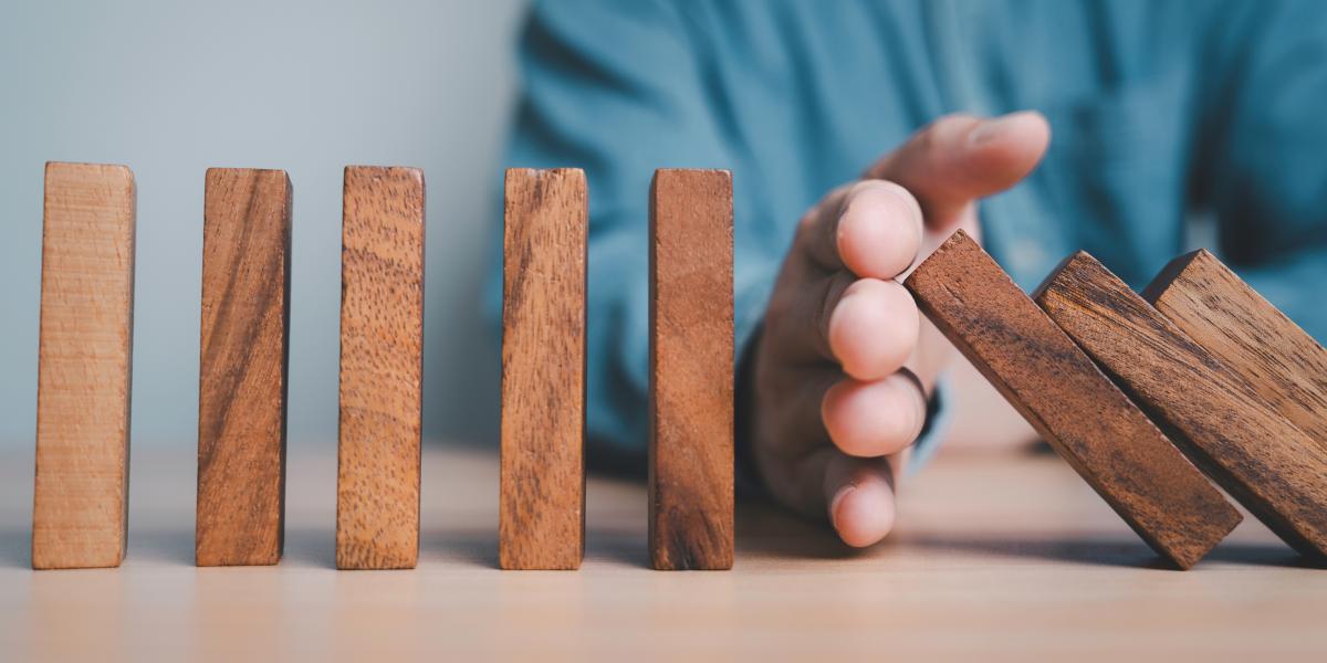 wooden blocks falling domino style, with hand stopping some from falling