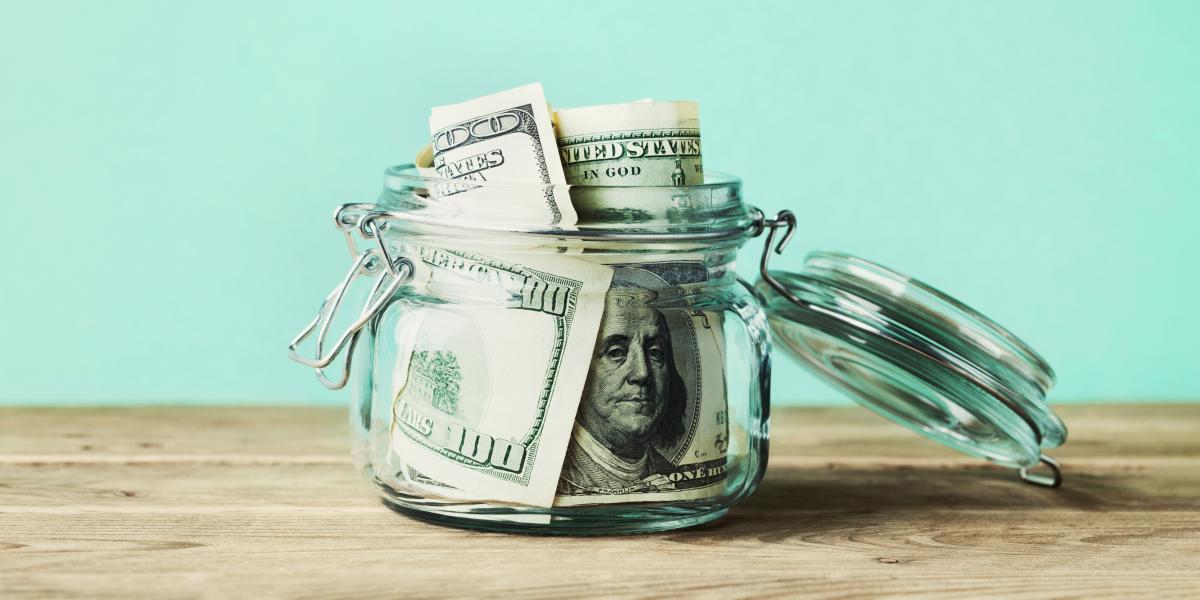 dollar bills in glass jar on wooden table