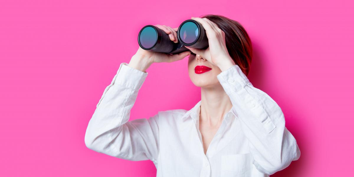 Woman looking through binoculars against a pink background