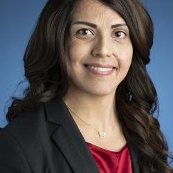 Maria Melendrez is in front of a blue background wearing a red shirt