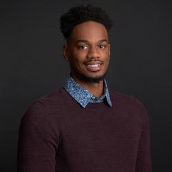 Vaughn smiles in front of a dark background, wearing a red sweater