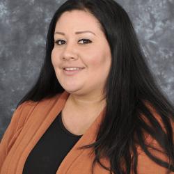 Woman with long dark hair, wearing an orange sweater against a gray background