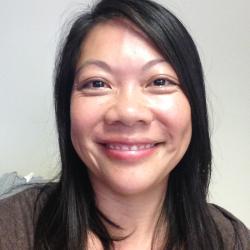 Close up of woman with long black hair, wearing a brown top, against a white background