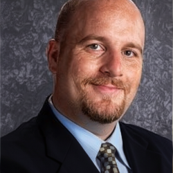Shaun smiles in a suit and tie headshot