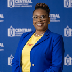 Toyin wearing a blue blazer with a yellow shirt under it. 