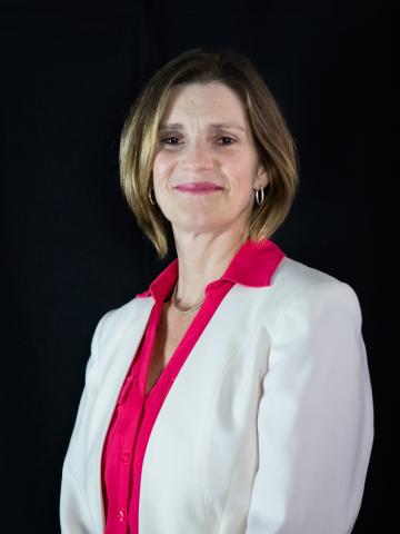 a women with dirty blonde hair, slightly shorter than shoulders, wearing a white blazer and a pink shirt