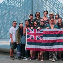 Students hold a Hawaiian flag in front of the Louvre museum.