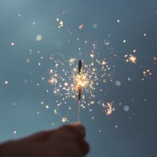 hand holding lit sparkler against dark blue backgorund