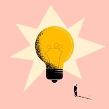 small figure stands looking up at big light bulb