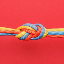 photograph of orange, blue, and yellow cords tied in knot on red background