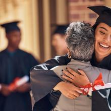 young smiling woman in cap and gown hugs older woman