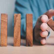 wooden blocks falling domino style, with hand stopping some from falling