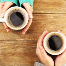 Two people holding cups of coffee on a table