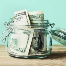 dollar bills in glass jar on wooden table